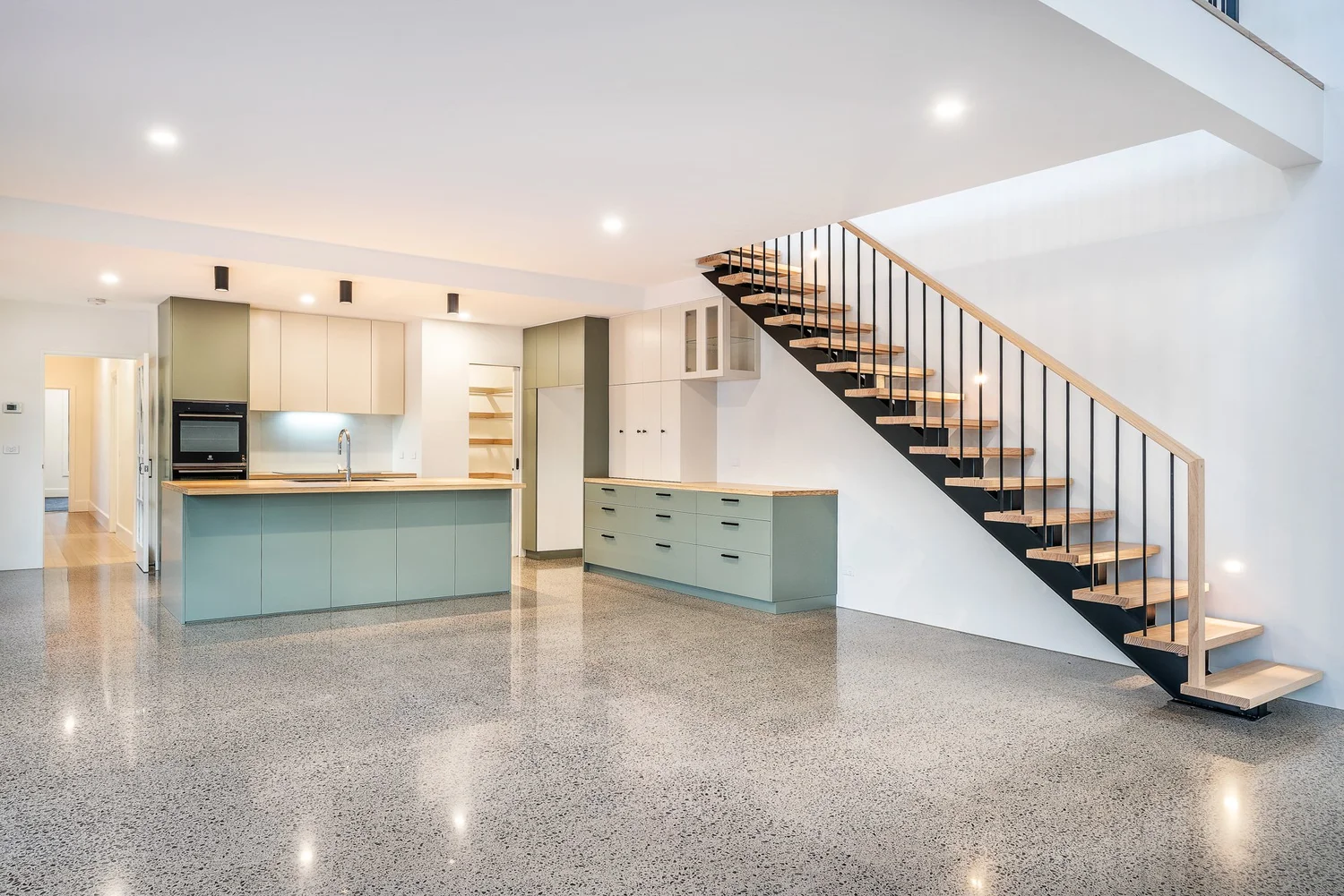 Open-plan living with floating timber staircase, sage kitchen island and polished concrete floor, Colin Street Bentleigh East — Eco Building Design