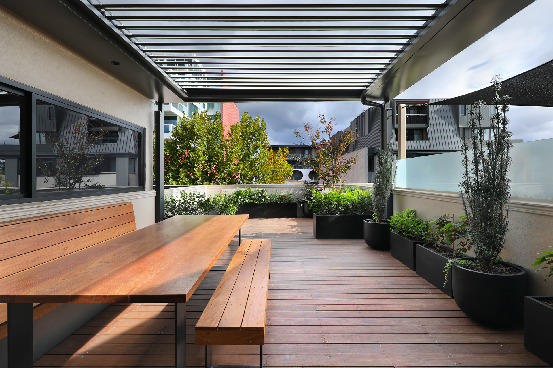 Rooftop terrace with timber table and benches under the louvre pergola, George Street Fitzroy